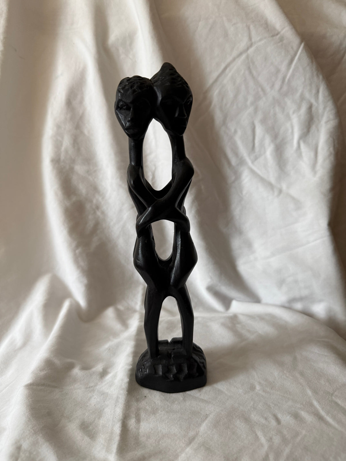Dark carved wood sculpture of two figures back to back